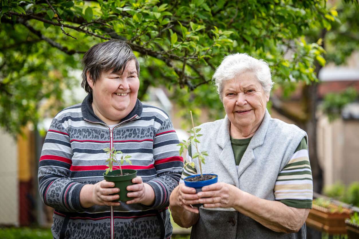 senior and younger woman with autism holding a tomato seedling in their hands and smile. concepts like inclusion and independent living